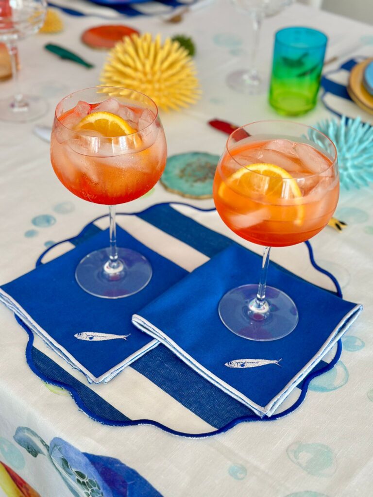 Per un Ferragosto al mare la tavola di Mònica @latavolacolorata si presenta con due coppe di Aperitivo leggermente alcolico su uno sfondo di decorazioni a soggetto marino
